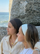 Two women sitting by a stone wall with ocean view